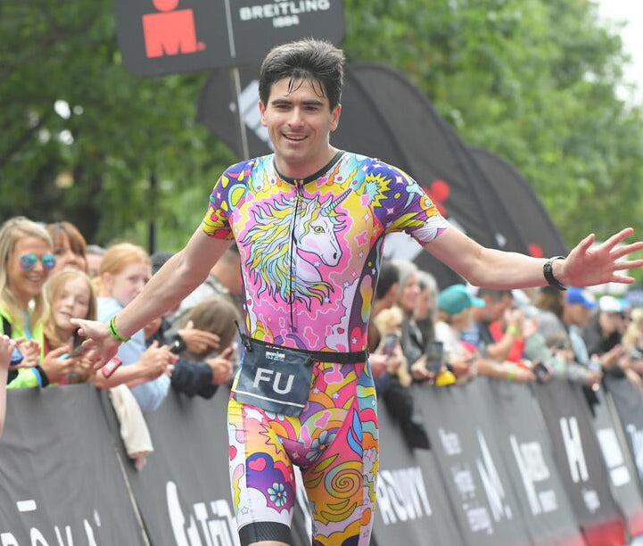 Athlete in colorful racing suit crossing finish line with crowd and branding in background